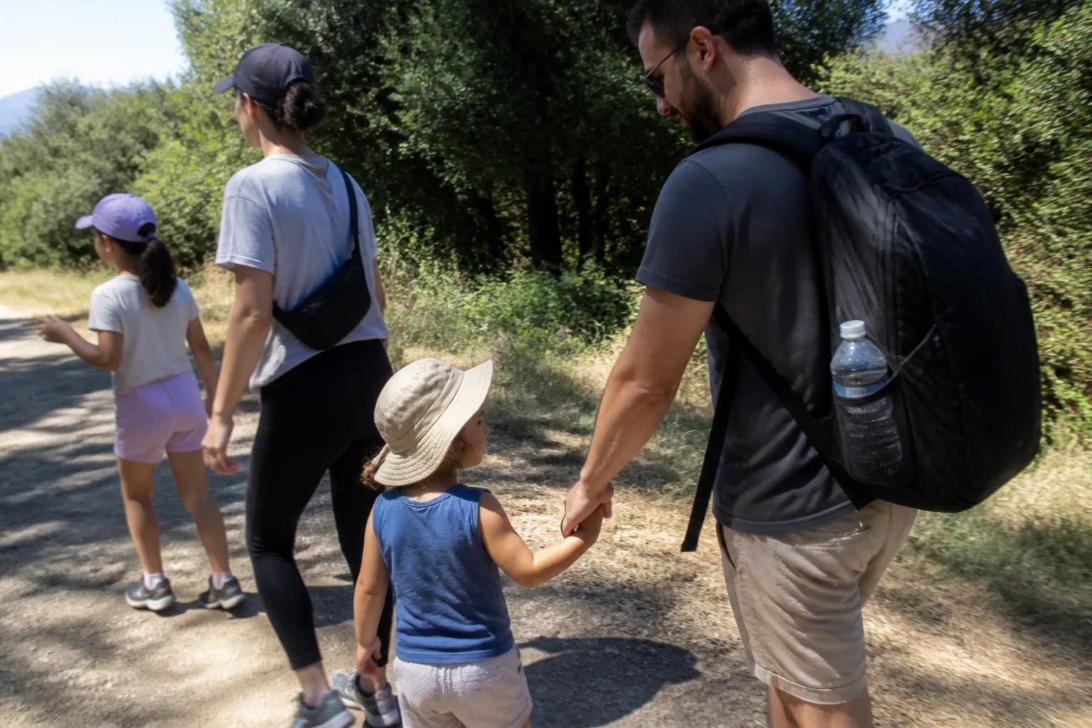 משפחה הולכת יחד בשביל חוץ ביום קיץ, ההורים מחזיקים ילד קטן ביד